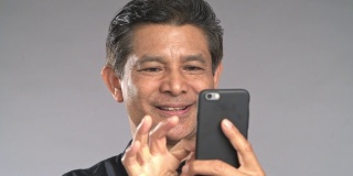 老人用手机浏览，很开心的微笑，孤立在灰色的背景中。穿着黑衬衫的亚洲人。