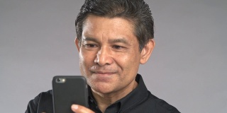特写的高级男子拍摄视频与他的手机孤立在灰色背景。穿着黑衬衫的亚洲人。