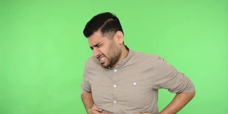 Stomachache. Sick brunette man suffering abdominal pain, bloated belly. studio shot, green background