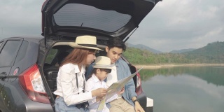 亚洲家庭的肖像坐在汽车与父亲指向的观点和母亲与女儿看美丽的风景和拿着地图在假期一起度假。幸福的家庭时间。