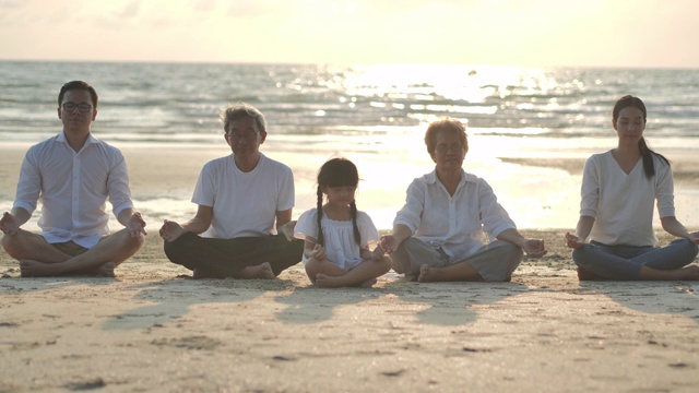 一个大家庭在沙滩上做瑜伽日落海浪的剪影。家庭，生活方式，人，人寿保险，多代人，老人，假期，关系，孩子，假期，退休，健康护理，领导理念。