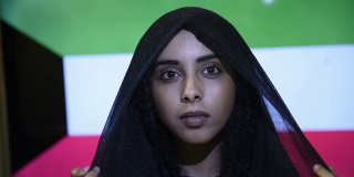 近距离观看年轻美丽的穆斯林女孩戴着头巾，站在科威特国旗前