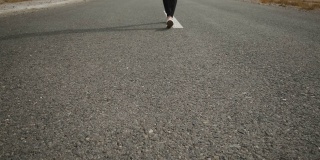 男人的黑色运动鞋与一个白色的鞋底走在灰色的柏油路上一个缓慢，标记的道路