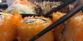 年轻的亚洲女人用筷子吃寿司，加州卷，日本食物