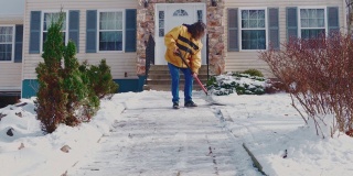 一名50岁的长头发男子，身穿黄色夹克，正在清理一场冬季降雪后乡间屋前院子里的积雪。科勒,宾夕法尼亚州,美国