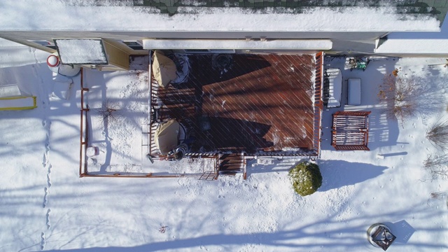 一名50岁的长头发男子穿着一件毛衣，在一场冬季降雪后清扫乡间房屋后院平台上的积雪。