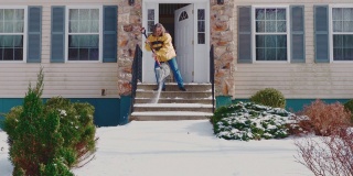 一个50岁的男人，长头发，穿着黄色夹克，正在清理一场冬季降雪后的门廊和楼梯。科勒,宾夕法尼亚州,美国