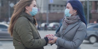 两个年轻的妇女在保护面具站在城市街道上聊天的特写。黑发女孩和她的蓝色头发的女性朋友讨论关于冠状病毒的最新消息。危险,流行。