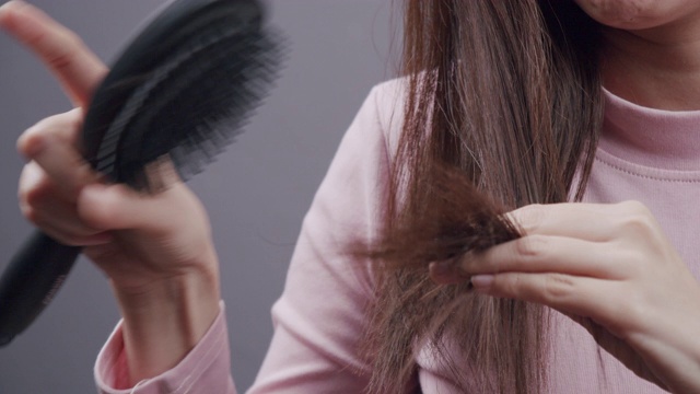 健康和美丽。有吸引力的亚洲女人或美丽悲伤的女孩与长损伤，散乱和凌乱的头发在她的手。头发护理的概念。高分辨率。