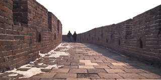 一对夫妇一起探索中国的长城，低镜头在宽阔的通道的石头路面上。冬天，游客们手牵手下来，欣赏空荡荡的慕田峪景区