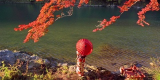 一名亚洲妇女穿着日本传统和服和红伞站在红枫树叶或秋天的叶子在岚山河在秋天的季节，日本京都旅游度假旅行。