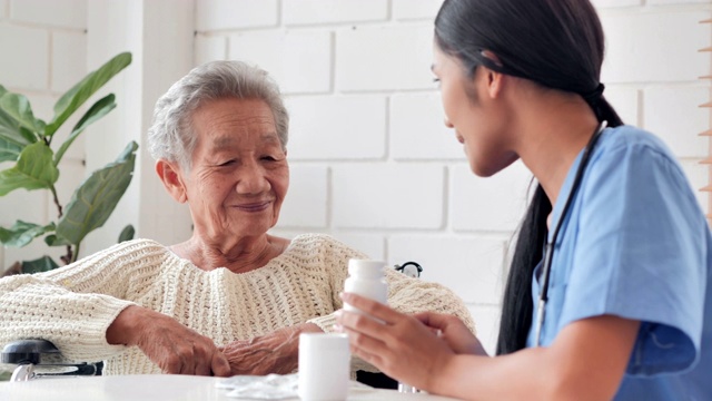 亚洲老年妇女听年轻的黑人女护士医生解释药物给她年长的女性病人在家。采购产品医疗，护理，护理，退休，志愿者，慈善，教育，养老院，在家照顾者，医药和卫生保健