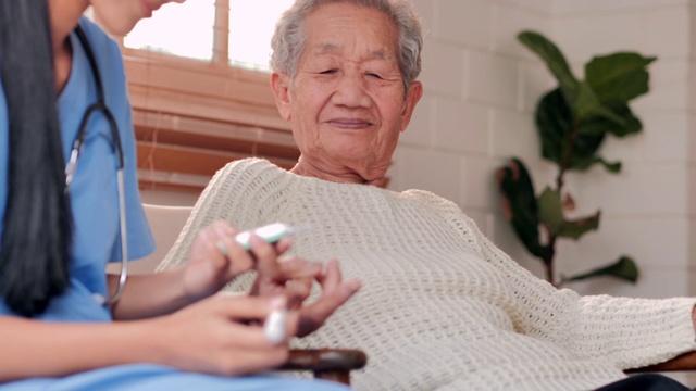 年轻的黑人女护士医生帮助患者亚洲老年妇女糖尿病正在做一个血糖水平手指血液测试，呆在家里防止冠状病毒或Covid-19的流行。老年人医疗保健、医疗、照顾、退休