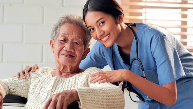 肖像快乐的志愿者年轻的黑人女性护士看护与亚洲老年祖母病人看着相机呆在家里防止新冠病毒或Covid-19的流行。医疗保健，护理，退休，家庭，慈善，养老院。