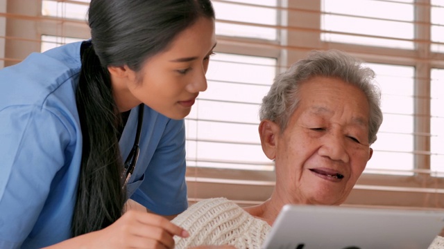 亚洲老年妇女与年轻的黑人女护士医生交谈，帮助患者在家里进行平板电脑治疗Covid-19病毒的教育。教育、医疗、护理、技术、老年护理、退休、志愿者、养老院、冠状病毒或Covid-19，家庭护理人员