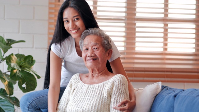 肖像快乐的志愿者年轻的黑人妇女护士看门人与亚洲老祖母说话，耐心的笑，在家里看着照相机。医疗、卫生保健、照顾、关心,退休,家庭,生活方式,志愿者,慈善,养老院的概念。