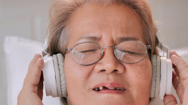 微笑的亚洲老年妇女坐在家里听音乐的肖像，防止。老年假期，技术，护理，人，退休，生活方式，医疗保健和医学，家庭概念。