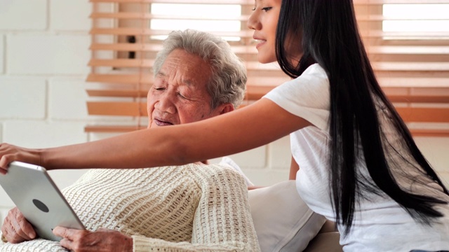 家庭护理人员:亚洲老年妇女与年轻黑人女性护理人员交谈，帮助患者通过平板电脑进行家庭Covid-19病毒医疗教育。教育，医疗，护理，技术，老年护理，退休，志愿者，慈善，养老院