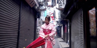 快乐年轻美丽的亚洲女性穿着传统的日本和服，手拿红纸伞微笑着走在日本东京新宿地区的街道上