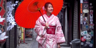 快乐年轻美丽的亚洲女性穿着传统的日本和服，手拿红纸伞微笑着走在日本东京新宿地区的街道上
