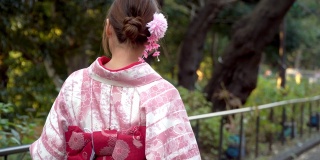快乐年轻美丽的亚洲女人女孩穿着粉红色的传统日本和服走在公园的街道上，看着远离东京城市，日本的4K后视图