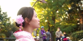快乐年轻美丽的亚洲女性女孩穿着粉红色的日本传统和服走在公园的街道上，环顾四周，微笑在日本东京城市