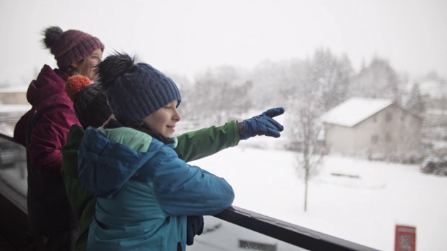 孩子们站在阳台上看雪。