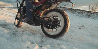 摩托车手在雪地上轮胎烧坏，慢镜头。夕阳西下，专业的摩托车手在雪地上滑行和转弯。骑摩托车的人在摩托车上表演特技