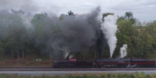 两辆蒸汽机车的空中侧视图，双头货运列车冒着黑烟和蒸汽