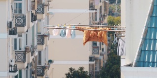 在阳光明媚的日子里，洗过的衣服挂在窗户外，背景是模糊的建筑物。中国典型的挂床单和挂衣服的生活方式。