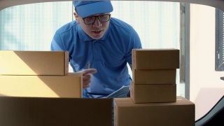 一名亚洲快递员，在快递车的后面检查和搬运纸包盒。邮政投递服务的概念。慢动作4k超高清。视频素材模板下载