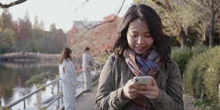 一名年轻女子拿着智能手机走在东京城市公园的街道上。