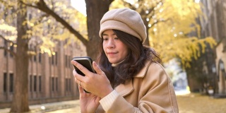在日本用秋叶背景的智能手机旅行的亚洲女性