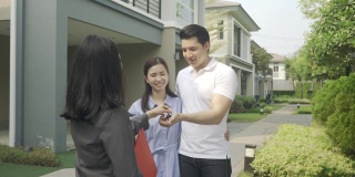 亚洲幸福的微笑年轻夫妇拿钥匙新大房子从房地产经纪人或房地产经纪人在他们的房子前签署合同协议后，房地产概念，搬家或出租财产