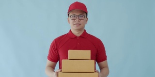 亚洲快乐快递员携带纸包盒子孤立在蓝色背景与微笑的脸。邮政投递服务的概念。