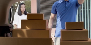 一名亚洲快递员在给女性顾客送货前，将纸包盒子放在车后座上检查并搬运。邮政投递服务的概念。4 k UHD。