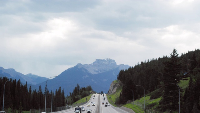 车辆行驶在横跨加拿大高速公路下的阴天与森林和加拿大落基山脉的背景在阿尔伯塔，加拿大