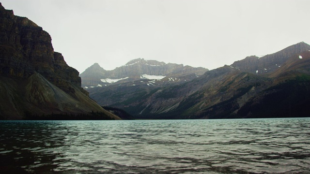 慢动作拍摄的山湖轻轻地荡漾和水花与加拿大落基山脉的背景在贾斯珀国家公园下的阴天在阿尔伯塔，加拿大