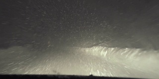 司机POV在积雪覆盖的道路上行驶，初雪飘落。被前灯和雪照亮的路。