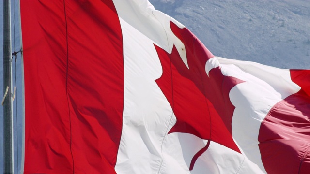 特写，慢动作镜头的旗帜加拿大吹在风与山的背景在一个阳光明媚的日子