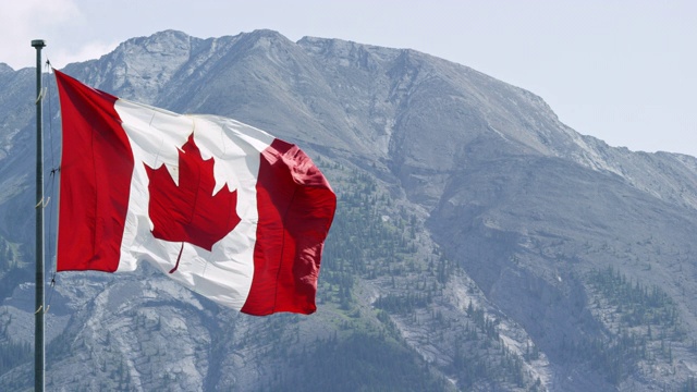 加拿大国旗在风中吹动的慢动作镜头与山在一个阳光明媚的日子的背景