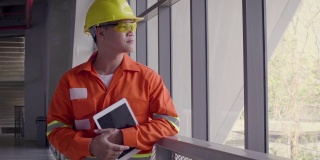 亚洲建筑或电子工程师的肖像，戴安全帽，穿着安全夹克，手持数字平板电脑旁边的窗户，工程师在工地检查建筑项目，看着相机