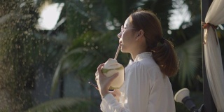 年轻的亚洲女人喝椰子水在日落，阳光周末公园