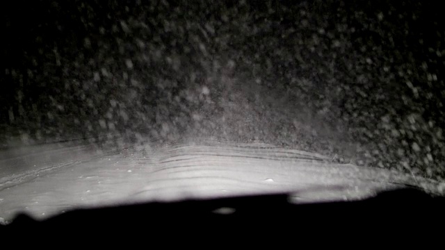 司机POV在积雪覆盖的道路上行驶，初雪飘落。被前灯和雪照亮的路。