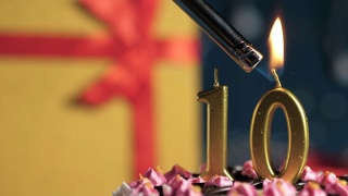 10号生日蛋糕用金色蜡烛点燃，蓝色背景的礼物用红色丝带绑在黄色盒子里。特写和慢动作视频素材模板下载