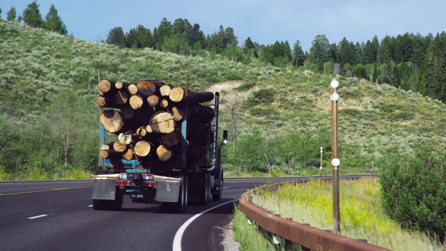 在一个阳光明媚的日子里，一辆满载原木的卡车在怀俄明州山区的高速公路上缓慢行驶