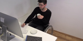 坐着轮椅的办公室职员，深色头发的女人在电脑旁边的工作场所喝咖啡，慢镜头