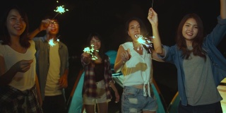 4K超高清慢动作:一群亚洲朋友在夏天的海滩露营庆祝与烟花灯在晚上。每个人都在快乐的跳舞，户外活动或度假。