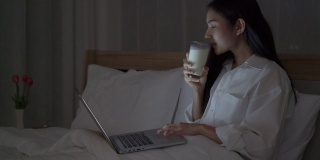 快乐的女人一边用笔记本电脑一边喝着牛奶