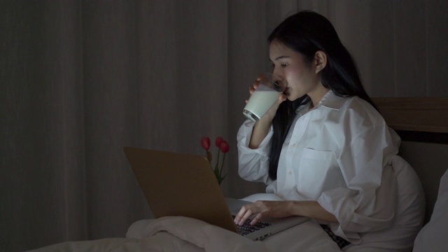 快乐的女人，晚上在笔记本电脑上工作，喝着牛奶